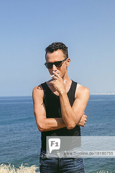 Man wearing sunglasses smoking cigarette in front of sea