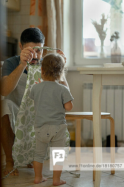 Vater trägt Schürze und kleiner Junge steht zu Hause in der Küche