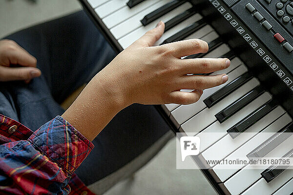 Hand of boy playing synthesizer at home