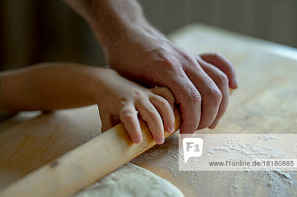 Hand eines kleinen Jungen und Vaters  der zu Hause in der Küche Pizzateig rollt
