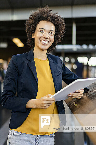 Happy businesswoman with tablet PC leaning on railing