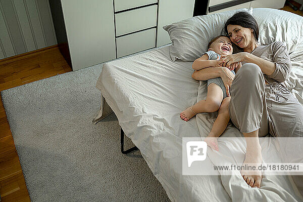 Glückliche Frau  die zu Hause mit ihrem Sohn im Bett spielt