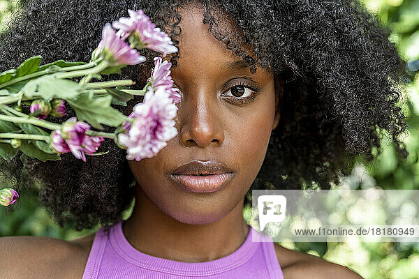 Young woman holding purple flowers in front of eye