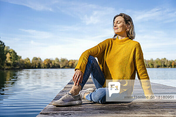 Smiling woman with eyes closed sitting at jetty on sunny day
