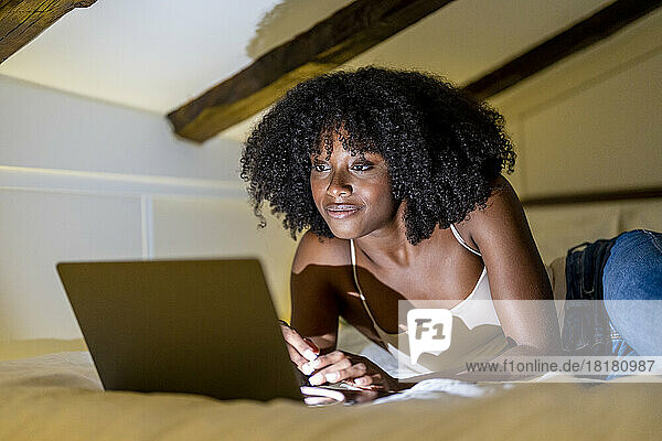 Afro woman watching movie on laptop in bedroom at home