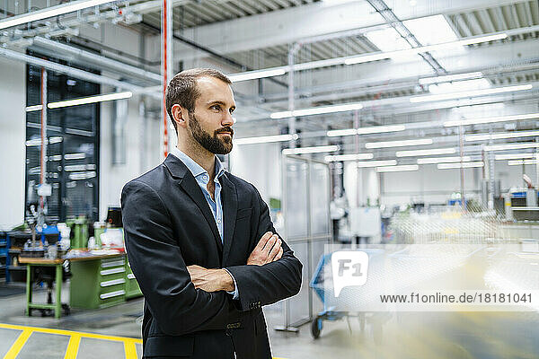 Contemplative businessman with arms crossed standing in factory