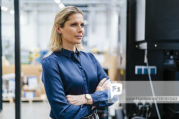 Contemplative businesswoman standing with arms crossed at factory