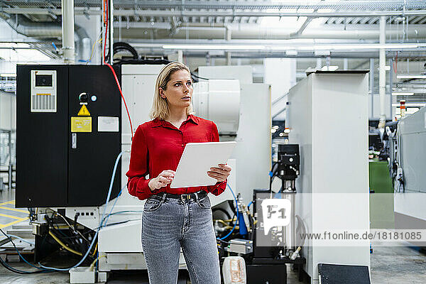 Thoughtful businesswoman with tablet PC standing in factory