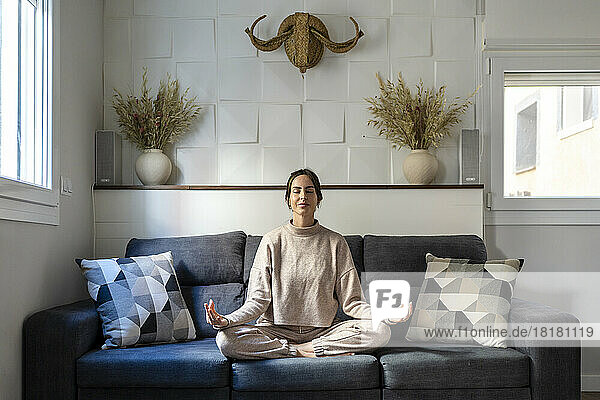 Young woman sitting on sofa meditating at home