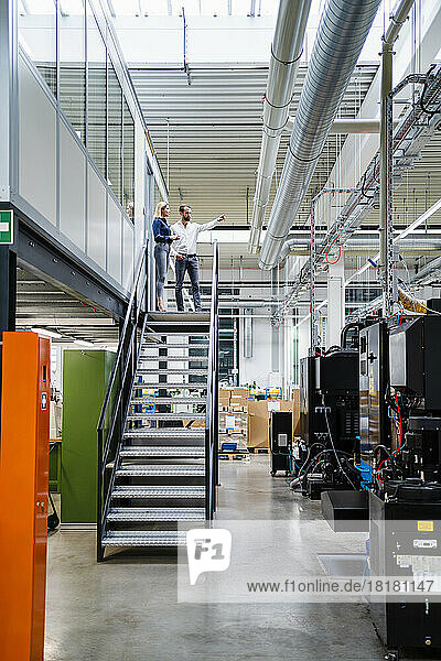Business colleagues discussing with each other standing on staircase in factory