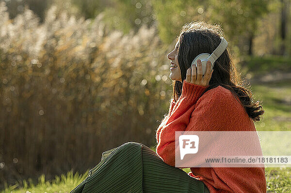 Glückliche Frau  die im Park Musik über kabellose Kopfhörer hört