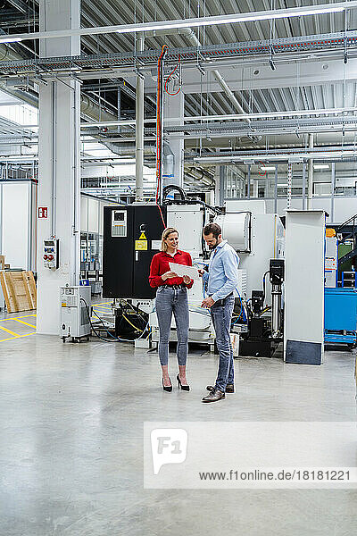 Geschäftsfrau hält Tablet-PC in der Hand und diskutiert mit Kollegen in der Fabrik