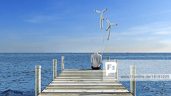 Invisible person sitting at edge of jetty with wind turbine shaped balloons in hand