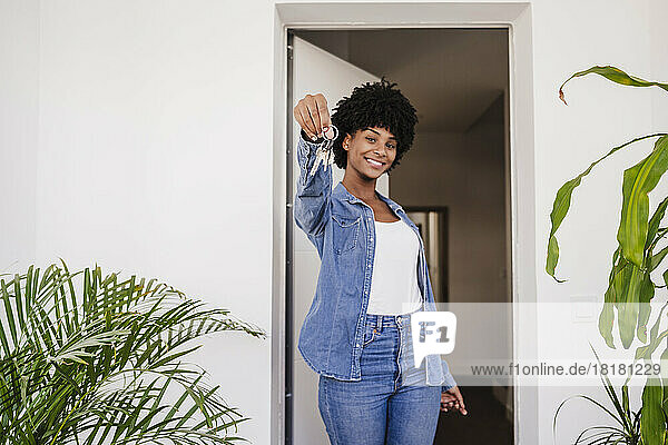 Happy young woman showing house keys standing in doorway