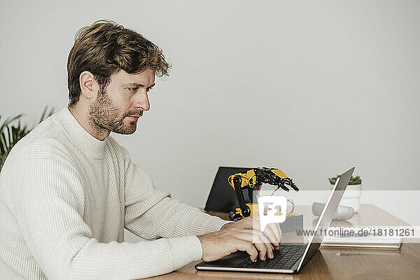 Businessman typing on laptop by robotic arm at workplace