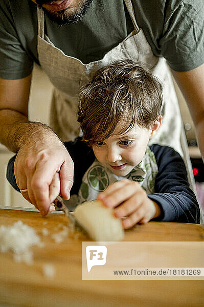 Son learning to chop onion from father in kitchen at home