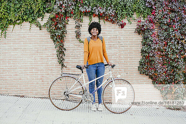 Smiling woman with bicycle in front of ivy wall