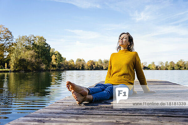 Happy woman with eyes closed sitting on jetty