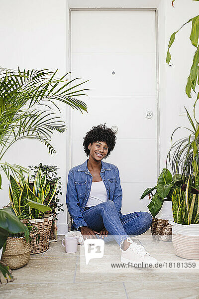 Glückliche Frau mit Kaffeetasse  die inmitten von Pflanzen sitzt