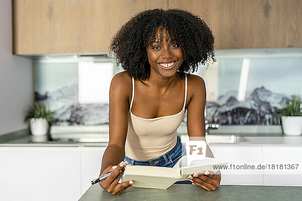 Afro woman with book leaning on kitchen island at home