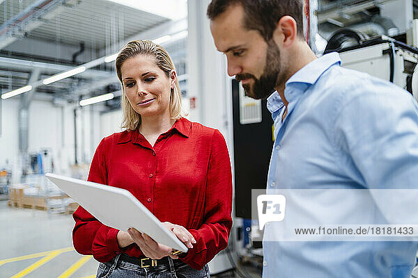 Smiling businesswoman sharing tablet PC with colleague at factory