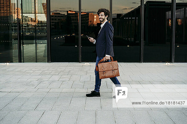 Businessman with briefcase walking on footpath by modern building