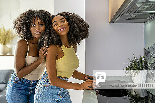 Young lesbian couple with cooking pan on glass stove at home