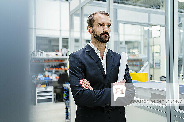 Contemplative businessman with arms crossed holding document at factory