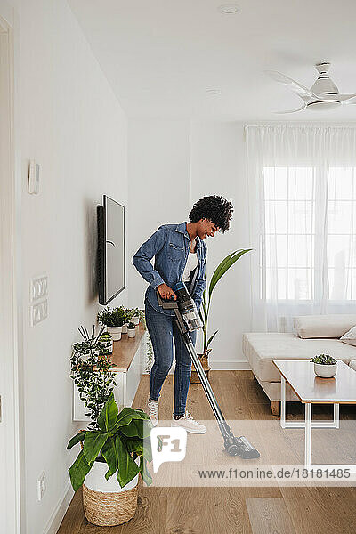Frau reinigt Wohnzimmer mit Staubsauger zu Hause
