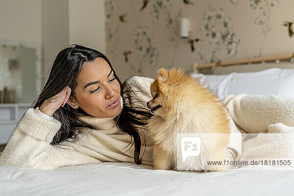 Smiling young woman with cute dog on bed at home