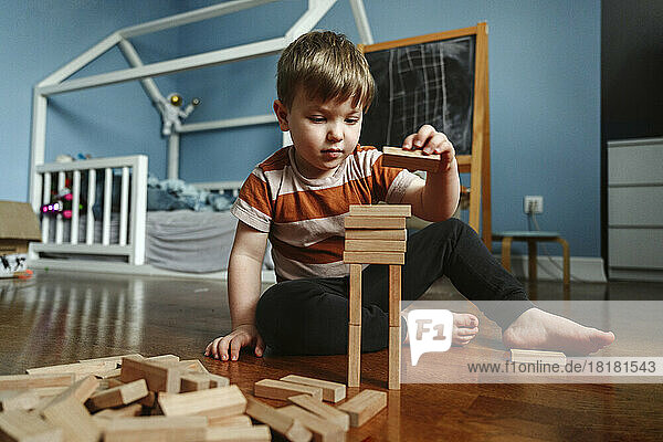 Junge spielt mit Holzklotz im Schlafzimmer zu Hause