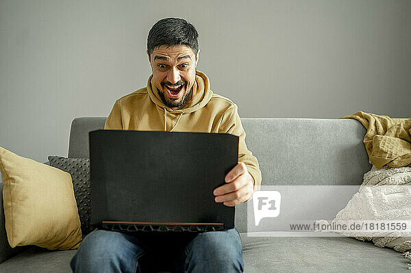 Surprised man using laptop sitting on sofa at home