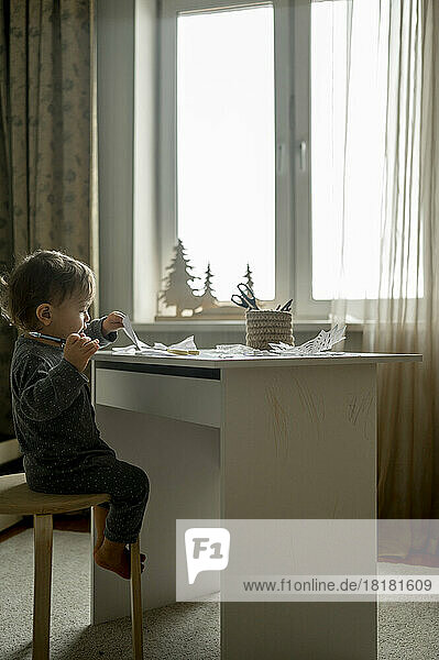 Junge sitzt zu Hause mit Papier und Bleistift auf einem Hocker
