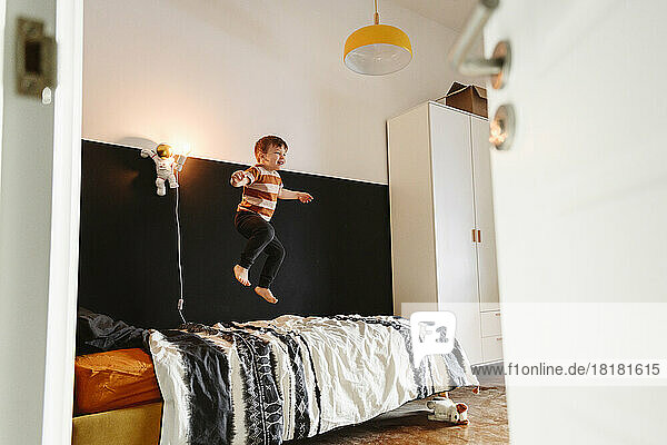 Playful boy jumping on bed in bedroom