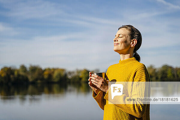 Smiling woman with coffee cup standing under sky