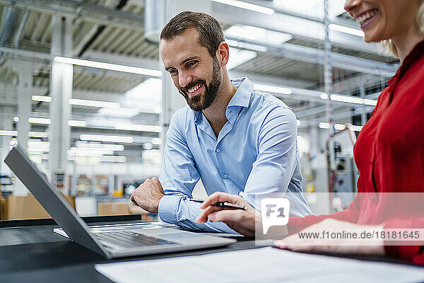 Happy businessman with colleague using laptop at factory