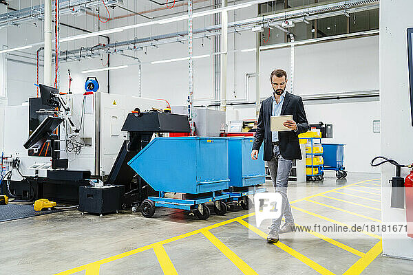 Businessman with tablet PC walking on markings in production hall at factory
