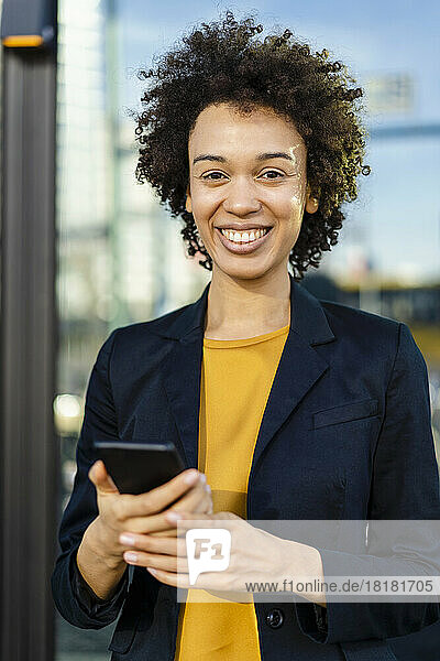 Smiling businesswoman wearing blazer holding mobile phone