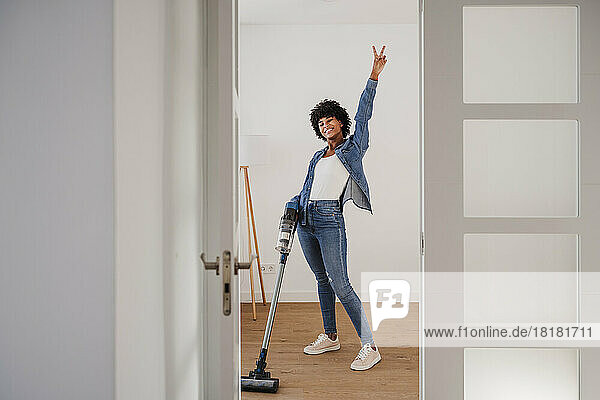 Happy young woman cleaning living room with vacuum cleaner