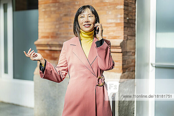 Glückliche junge Frau  die an einem sonnigen Tag über ihr Mobiltelefon spricht