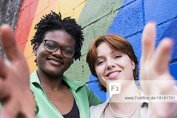 Smiling woman with friend gesturing in front of colorful wall