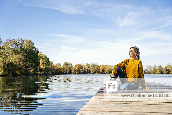 Frau sitzt auf Steg vor See