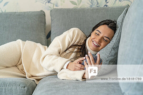 Glückliche junge Frau  die zu Hause auf dem Sofa ihr Smartphone benutzt