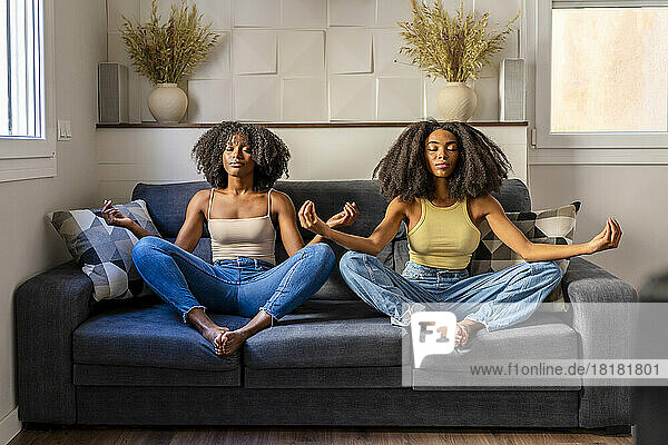 Young lesbian couple meditating on sofa in living room