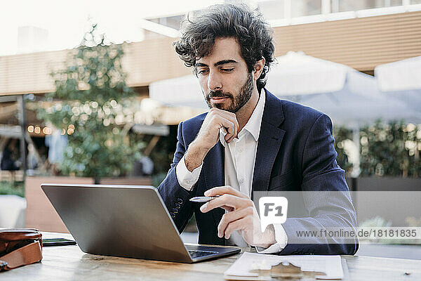 Konzentrierter Geschäftsmann mit der Hand am Kinn und Blick auf den Laptop