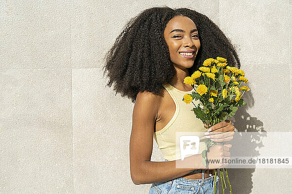 Smiling woman holding yellow flowers in front of white wall
