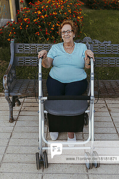 Smiling senior woman in front of walker sitting on bench