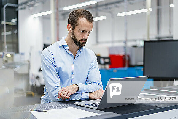 Konzentrierter Geschäftsmann beobachtet Laptop in der Fabrik