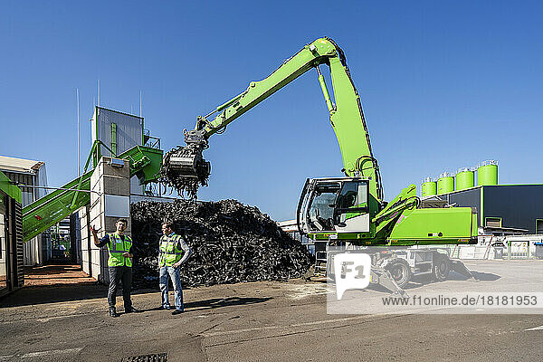 Man standing and discussing in front of excavator at recycling center