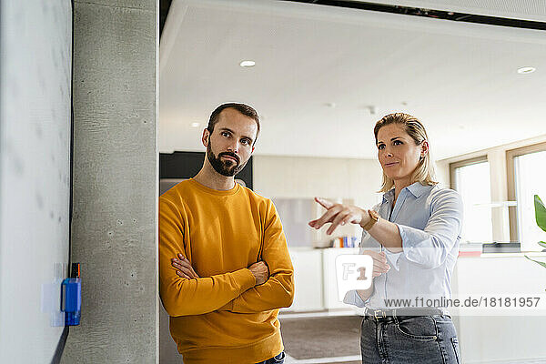 Businesswoman gesturing and talking with colleague leaning on wall at office